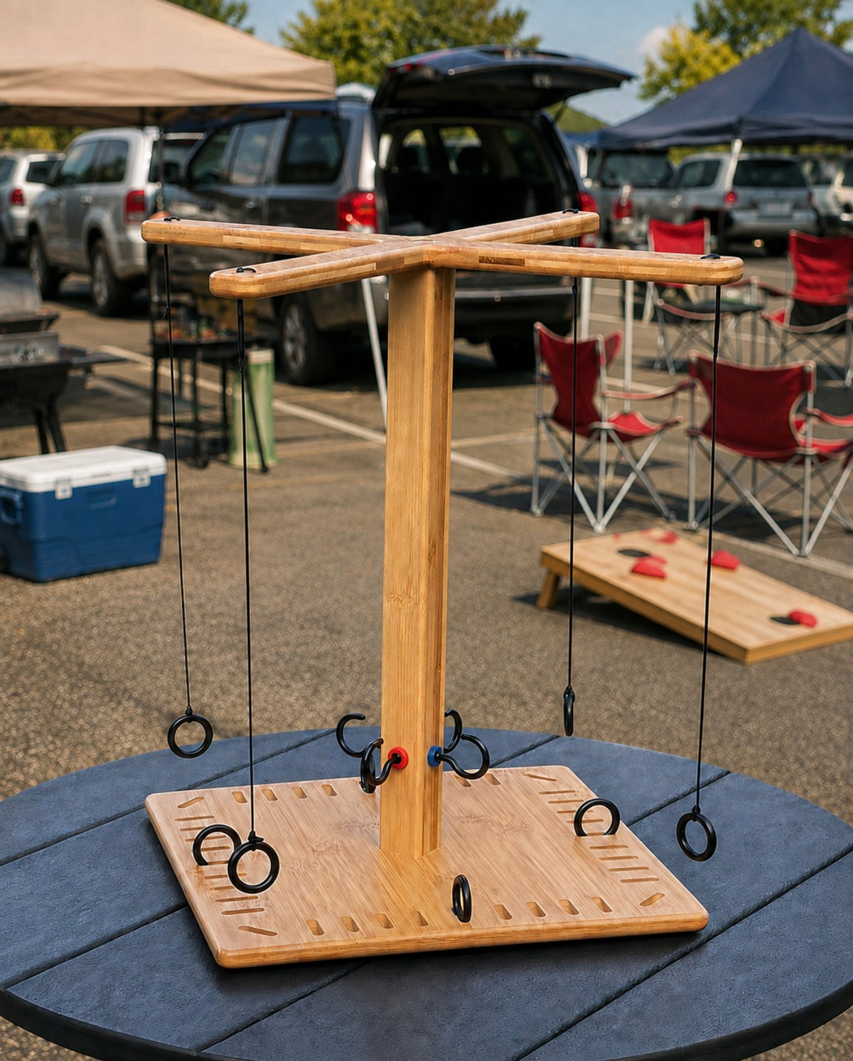 A wooden hanging ring game stand made of light natural wood, suspended over a square base with multiple black hanging rings, photographed outdoors at a park or event on a black table.